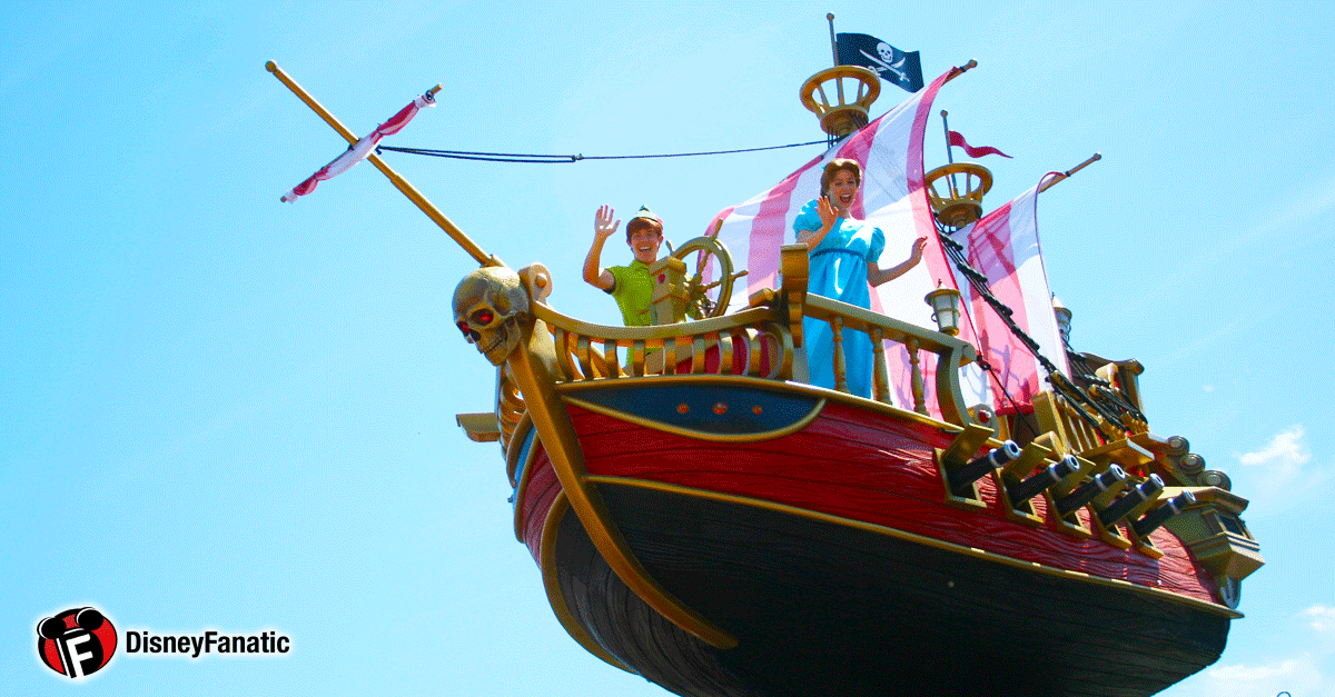 Peter Pan and Wendy greet guests from the Jolly Roger pirate ship float with pink sails at a Disney parade under a clear sky.