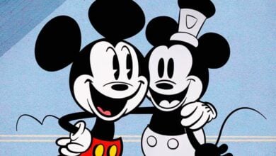 Two cartoon mice, reminiscent of iconic Mickey Mouse voice actors, stand close together smiling, one in red shorts and the other in a gray outfit with a hat, their arms around each other against a light blue background.