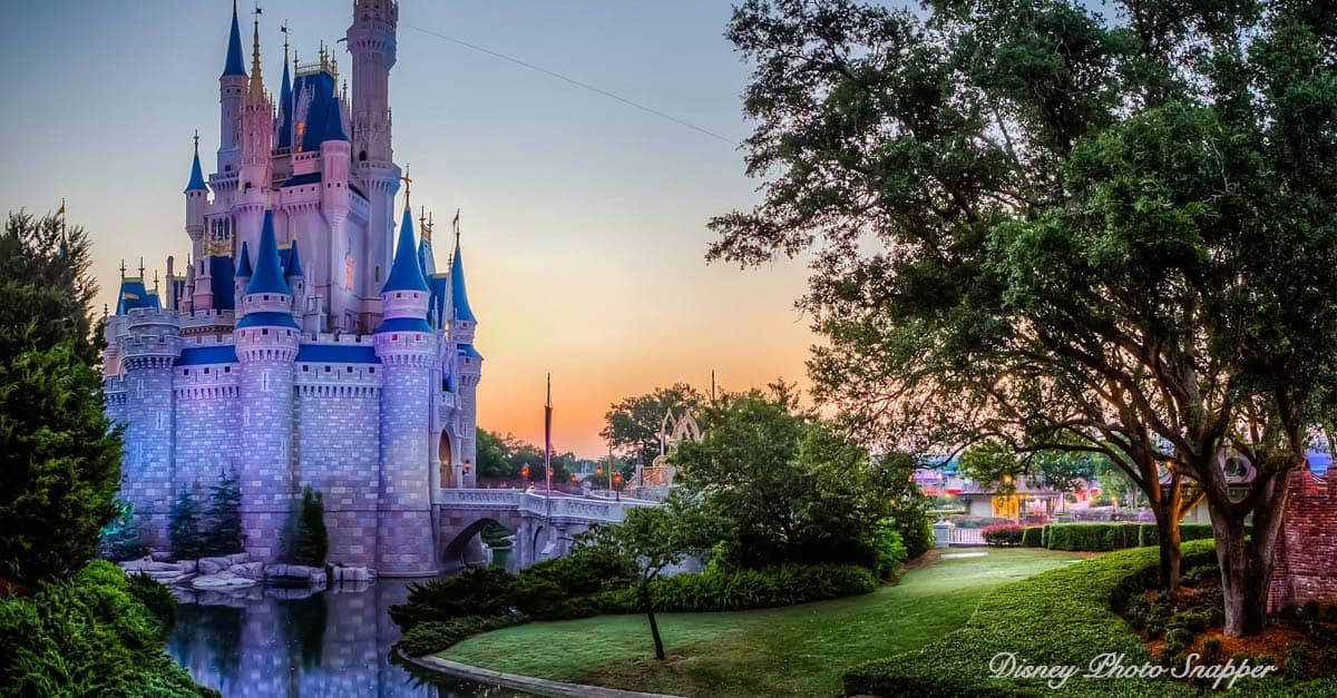 Cinderella Castle glowing at sunrise, framed by lush greenery and lawns in Magic Kingdom—a Disney fan’s dream vacation scene.