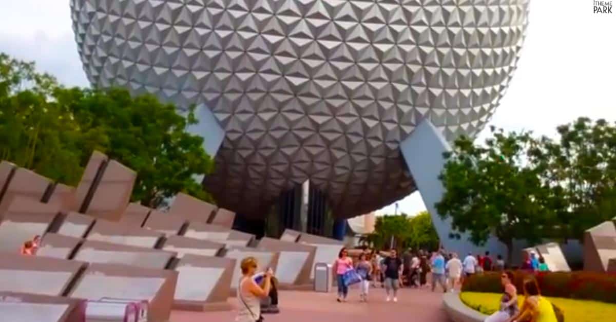 Guests stroll past Spaceship Earth in Epcot’s Future World, with Leave a Legacy plaques and lush greenery in the foreground.