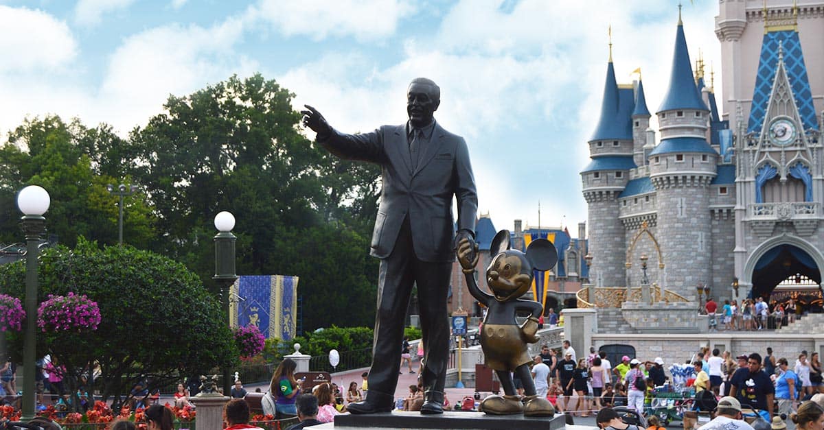 Walt Disney and Mickey Mouse statue in front of Cinderella Castle at Disney World, surrounded by crowds enjoying the magic.