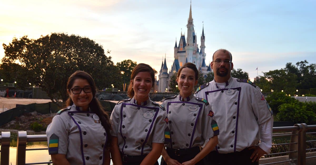 Cast Members in Disney uniforms beam with joy before Cinderella Castle at sunset, celebrating the enchantment of Disney Parks.