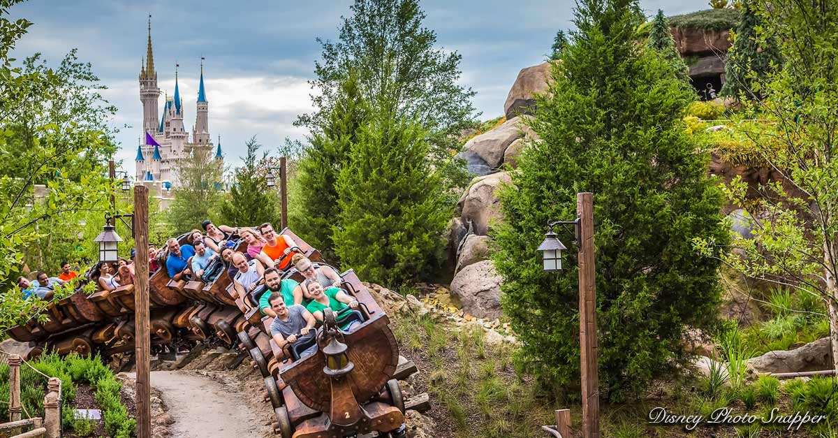 Thrill-seekers race on a Disney World coaster, surrounded by lush green scenery and the iconic castle in the backdrop.