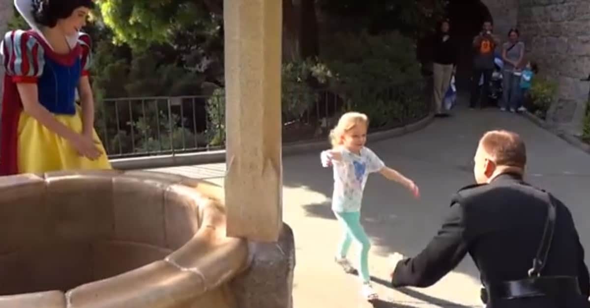 A young girl runs to her military dad near Disneyland’s wishing well, as Snow White greets guests nearby.