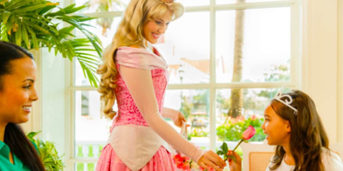 A Disney Princess presents a rose to a young guest in a tiara during a magical Princess Tea Party experience at Disney World.