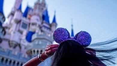disney guest wearing sparkling purple mickey ears in front of magic kingdom's cinderella castle