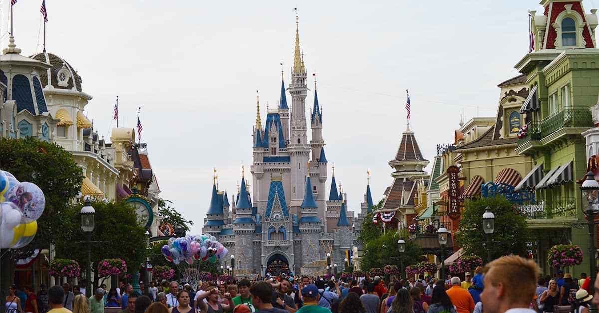 Guests flock toward Cinderella Castle at Magic Kingdom, passing vibrant storefronts and balloons—prime for unforgettable Disney adventures.
