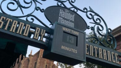 Entrance sign for The Haunted Mansion ride showing a wait time of 13 minutes, with decorative lettering and part of the attraction’s facade visible in the background—a fun find for Disney Ride Tips enthusiasts.