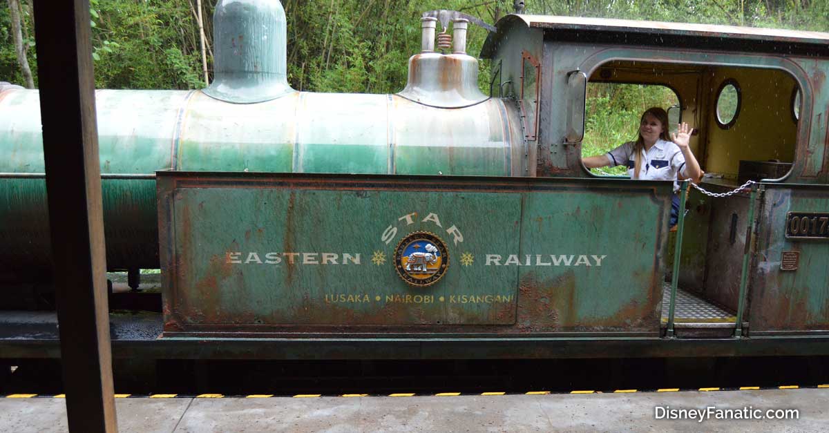 A friendly engineer waves from the cab of the green, weathered "Eastern Star Railway" train, greeting visitors like at a theme park.