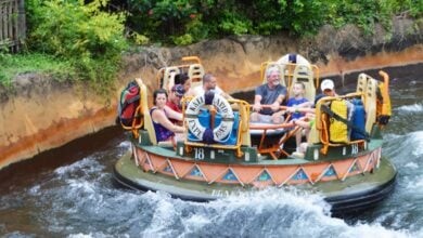 A group of people enjoying a river rapids ride in a circular raft. The raft navigates through whitewater surrounded by greenery. Everyone is wearing casual clothes and appears happy and excited as they hold onto the handles at Kali River Rapids at Disney World Animal Kingdom park.