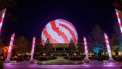 Spaceship Earth at Epcot glows in wintry style as swirling red and white lights illuminate the night. Tall columns echo the Disney World Winter magic, surrounding the circular plaza while trees frame this enchanting scene.