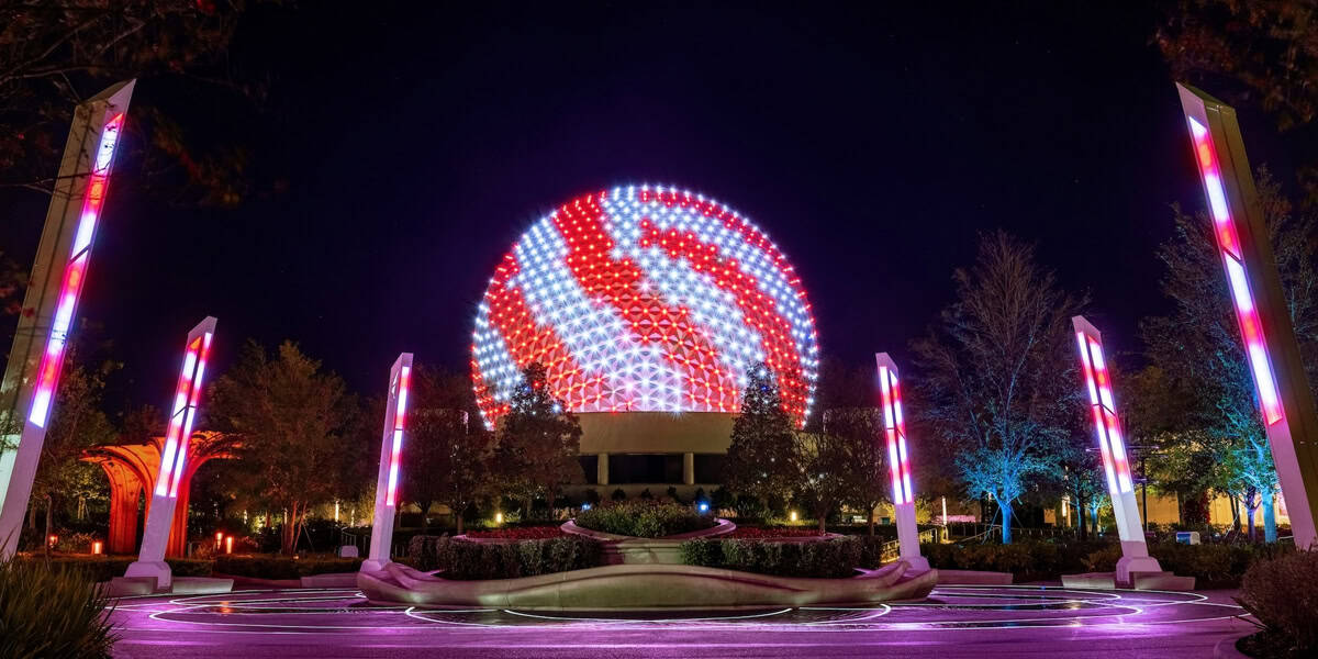 Spaceship Earth at Epcot glows in wintry style as swirling red and white lights illuminate the night. Tall columns echo the Disney World Winter magic, surrounding the circular plaza while trees frame this enchanting scene.