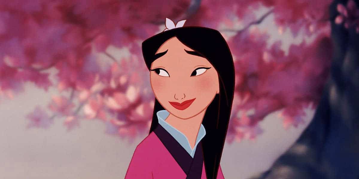 Mulan wearing a pink and blue outfit, stands in front of a backdrop of pink blossoms.
