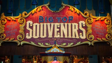 A colorful, circus-themed sign reads "Big Top Souvenirs" in large, lighted letters—a standout among Magic Kingdom shops—with banners on each side advertising "The World's Best Amazing Gifts" and "The World's Tastiest Treats.