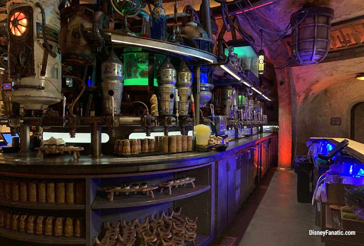 Step into Starport Lounge at Galaxy Quest Adventure Park, where glowing neon lights illuminate a futuristic bar filled with metallic pipes and high-tech drink dispensers, immersing guests in a sci-fi universe.