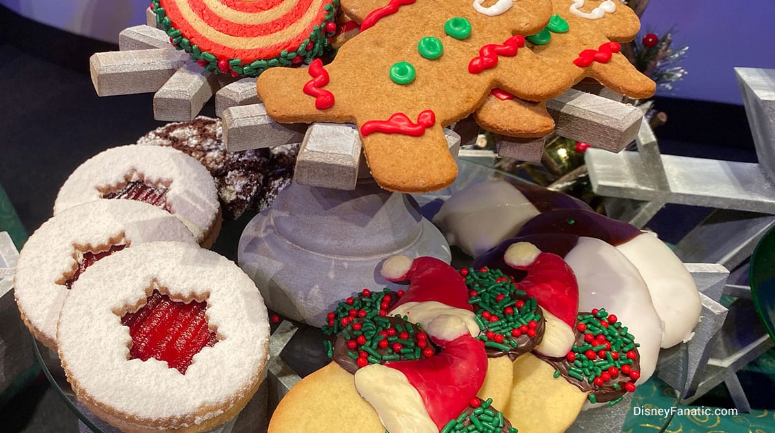 A festive tray of holiday cookies at a theme park, featuring gingerbread men, Linzer stars dusted with powdered sugar, and whimsical Santa hat treats—perfect for enjoying during seasonal celebrations at the park.