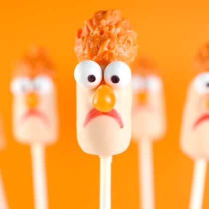 Beaker marshmallow pop featuring candy eyes, orange hair, and a sad face—just like at Muppet-themed parks and events.