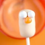 Beaker Cake Pop-inspired marshmallow treat with candy eyes and beak on a stick, ready for Muppet fans, pops against orange.