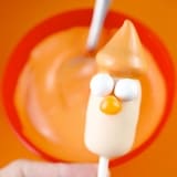 Beaker Cake Pop with whimsical hat stands ready for Muppet fans, displayed before a bowl of zesty orange icing.