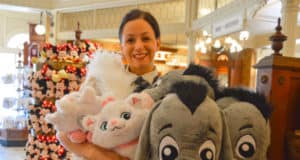 Guest beaming as she picks out giant plush toys in a lively Disney World shop filled with stuffed animals and souvenirs.