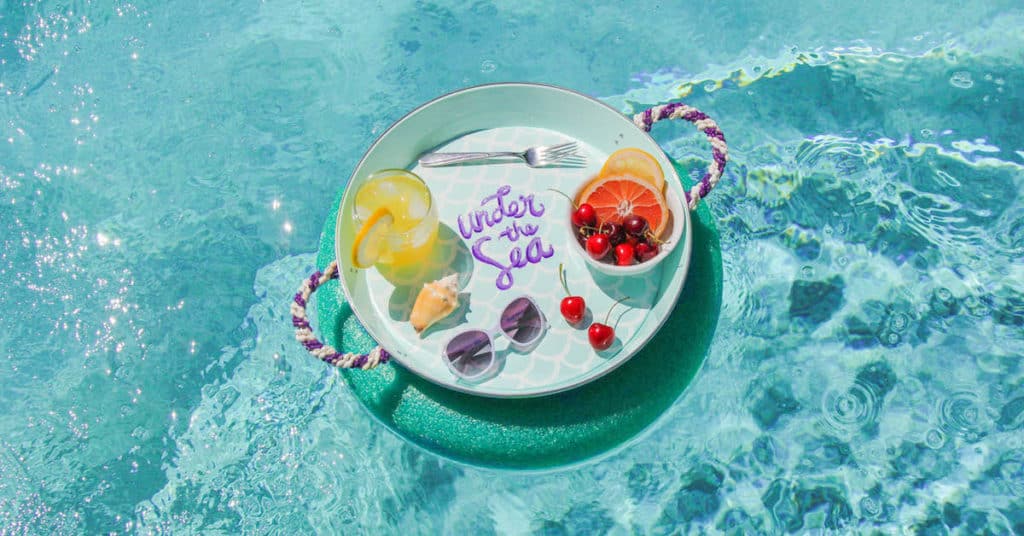 A themed pool tray with fruit, a tropical drink, shades, and an "under the sea" card floats—pure Disney magic vibes.