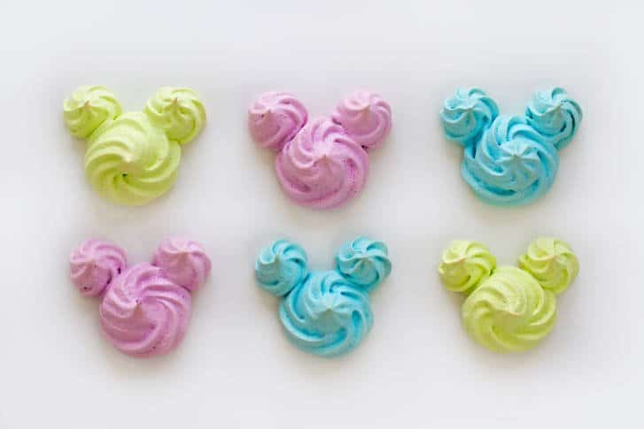 Colorful Mickey Mouse-shaped pastel meringues in green, pink, and blue bring Disney magic to a white display background.