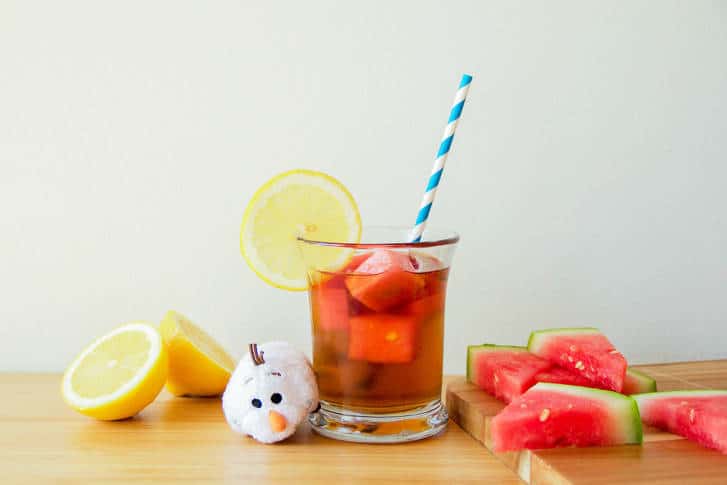 A refreshing glass of iced tea with lemon and watermelon ice cubes sits by Olaf at Disney’s Frozen-themed snack stand.