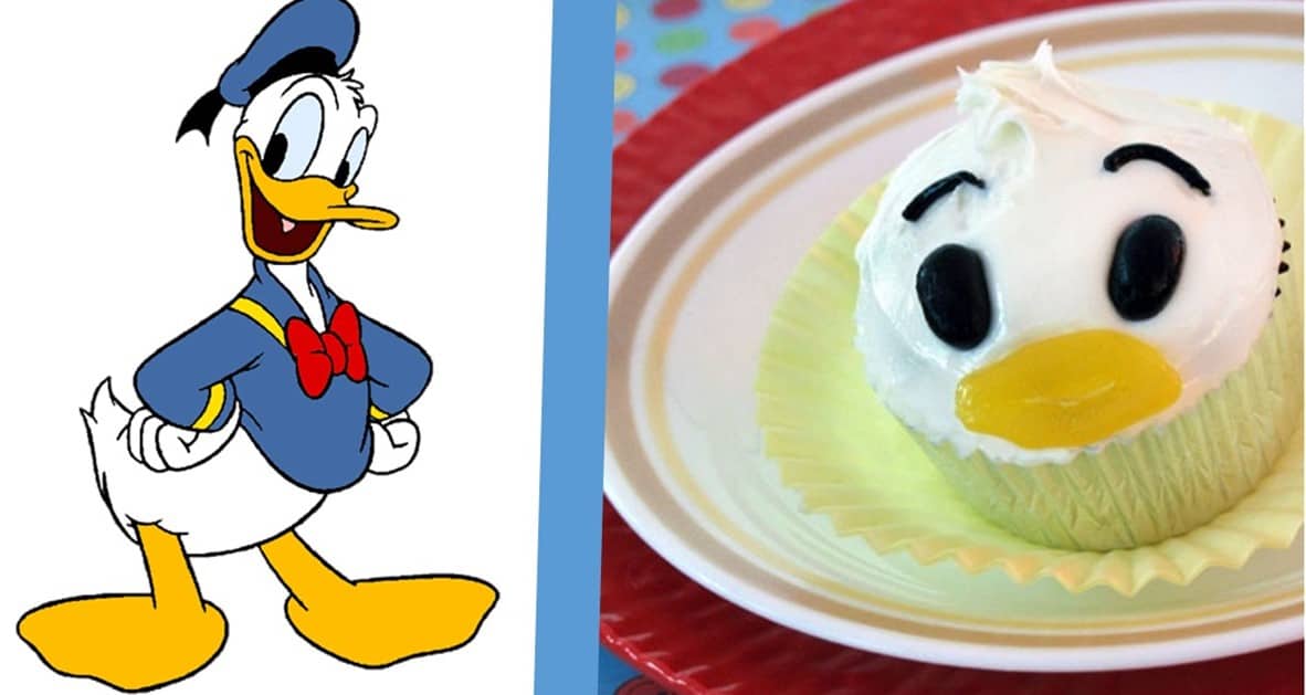Donald Duck in his classic sailor outfit stands next to a cupcake decorated exactly like his iconic face at Disneyland.