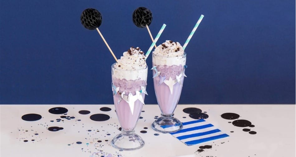Black Panther-inspired purple milkshakes with whipped cream and straws on a blue table—Wakanda treats at Disney’s Avengers Campus.