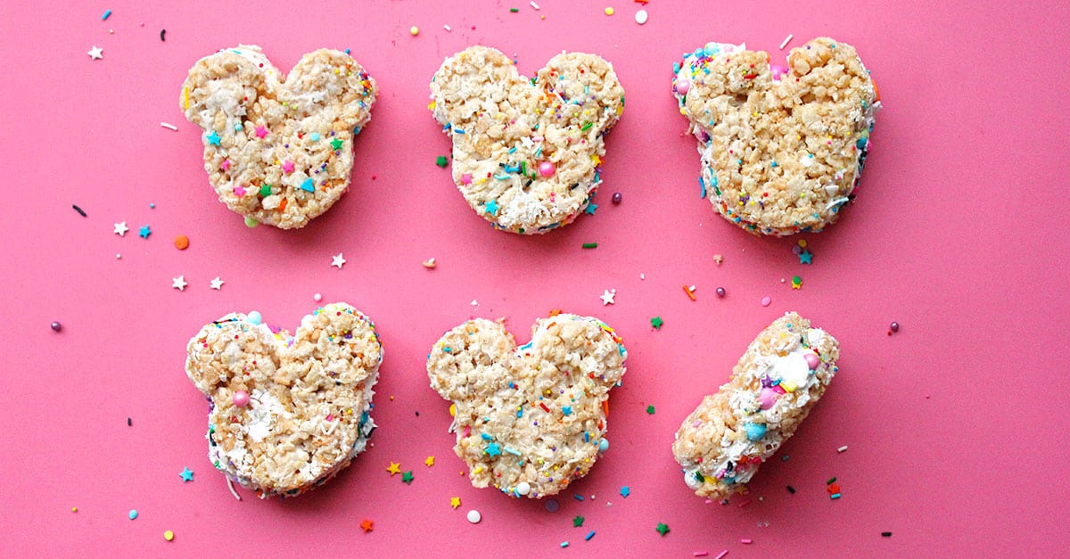 Six Mickey Mouse-shaped Rice Crispy treats with colorful sprinkles on a pink background, just like your favorite Disney parks snack.