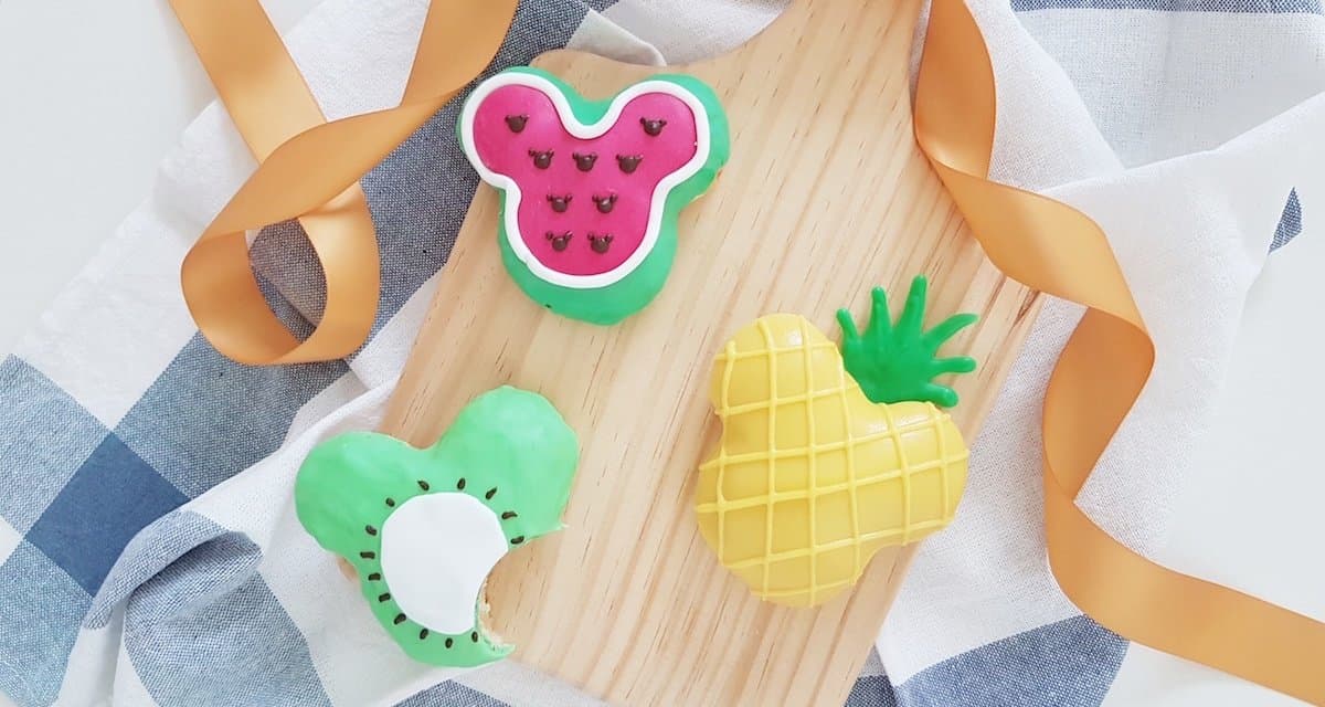 Three vibrant Mickey-shaped fruit cookies on a rustic board with ribbon—Disney Parks-inspired summer sweets from the iconic donut recipe.