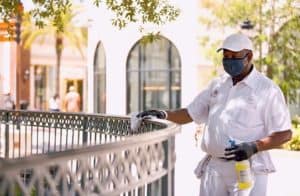 A masked Cast Member wipes down a railing with sanitizer and cloth, keeping Disney World safe and sparkling for guests.