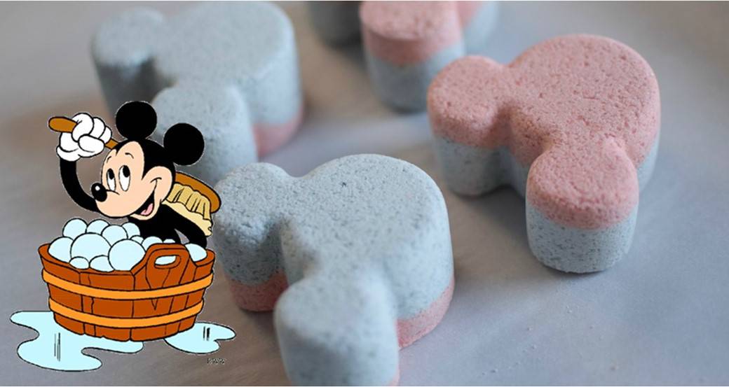 Pink and blue Mickey-shaped bath bombs for magical self-care, with Mickey Mouse cheerfully scrubbing a basket of bubbles nearby.