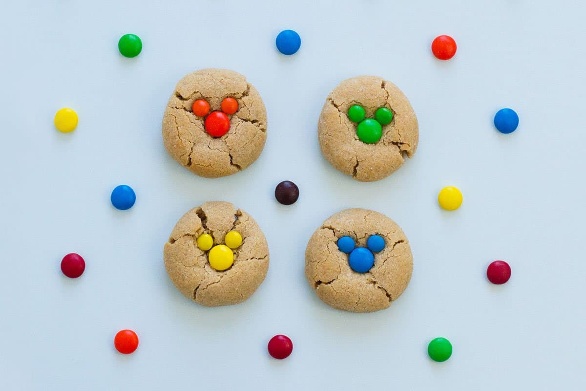 Mickey Mouse-shaped peanut butter cookies topped with colorful candies, surrounded by festive Disney-themed candy treats.