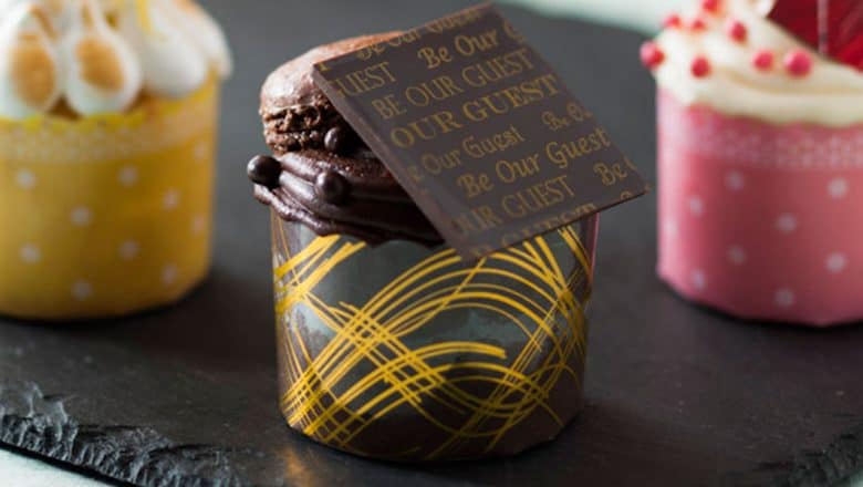 The Triple Chocolate Cupcake at Magic Kingdom, swirled in yellow, topped with a macaron and gold "Be Our Guest" chocolate.
