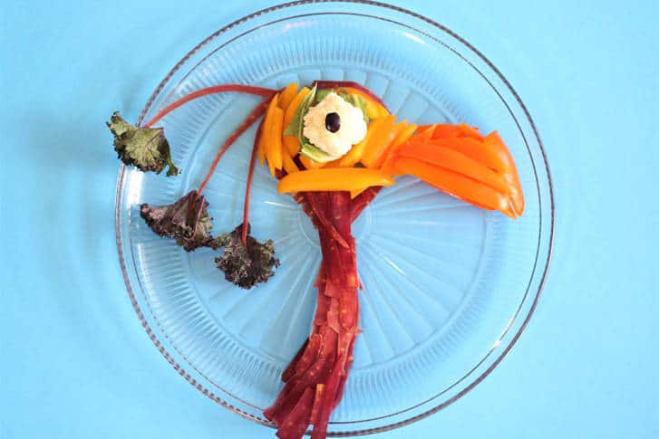 Kevin from Up recreated with vegetables on a plate, set against a blue backdrop—fun Disney-inspired food art for fans.