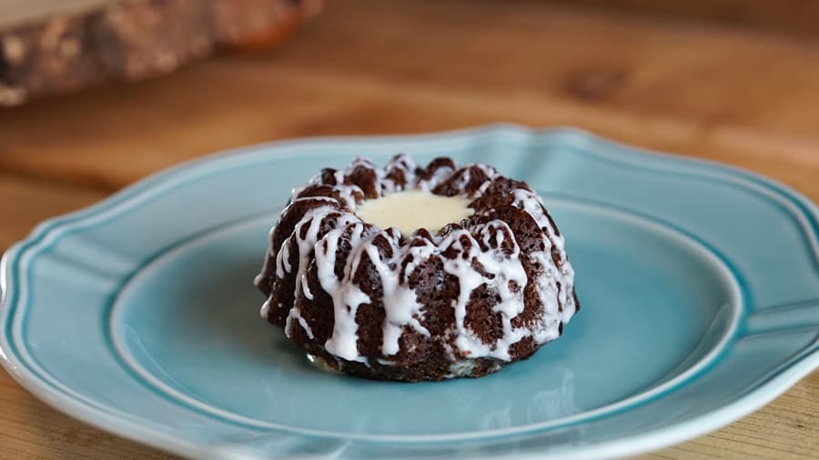 A Disney-inspired chocolate bundt cake with white icing on a blue plate, just like the treats found at your favorite parks.