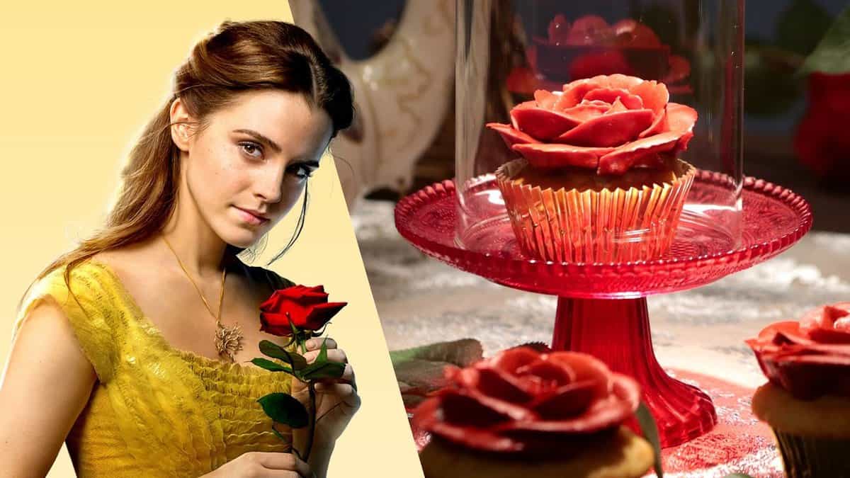 Belle in her iconic yellow gown holds a rose beside an Enchanted Rose Cupcake on a glass stand at the Disney park.