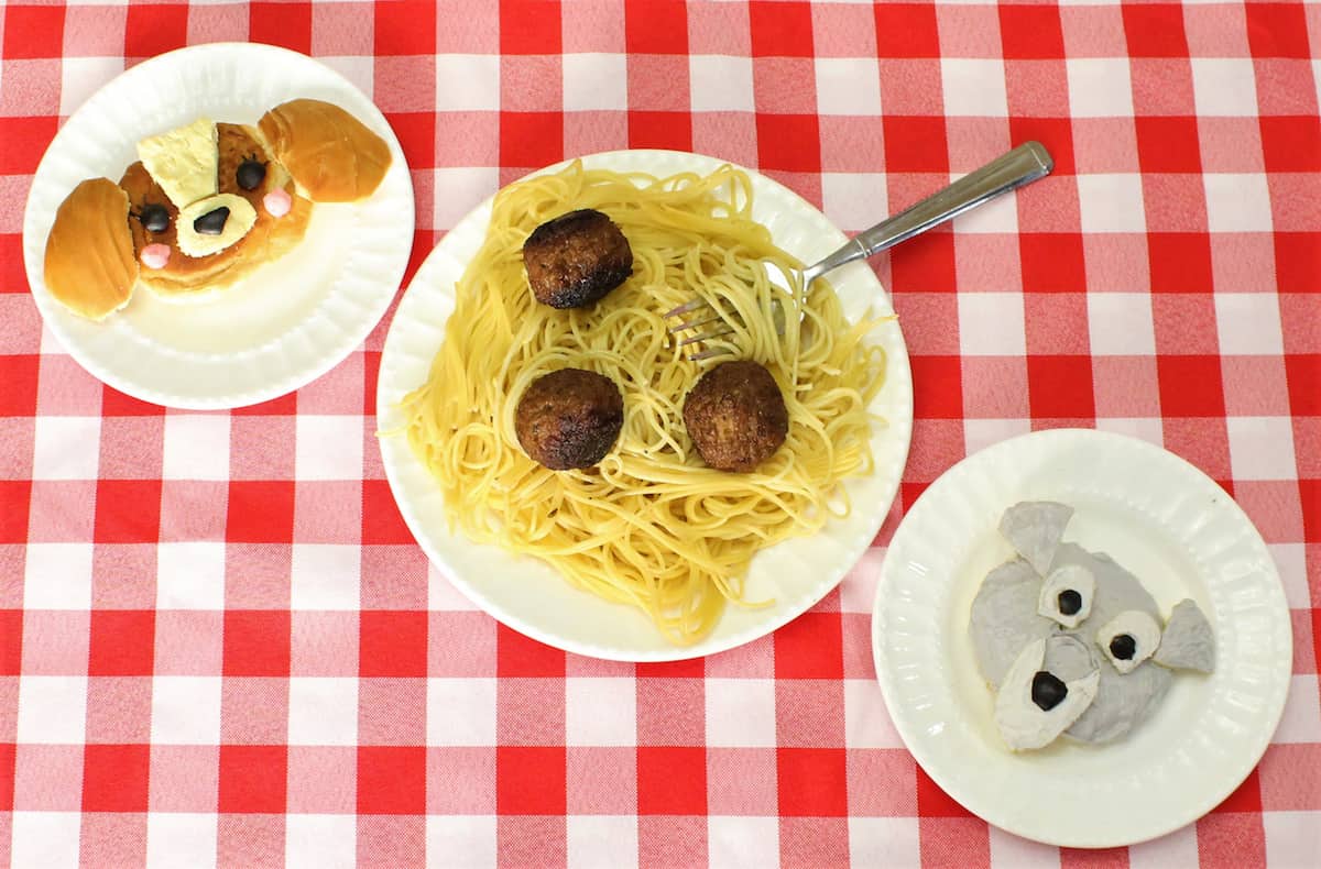 Three whimsical plates on a red checkered table: Lady and the Tramp-inspired spaghetti, plus two playful Disney animal face meals.