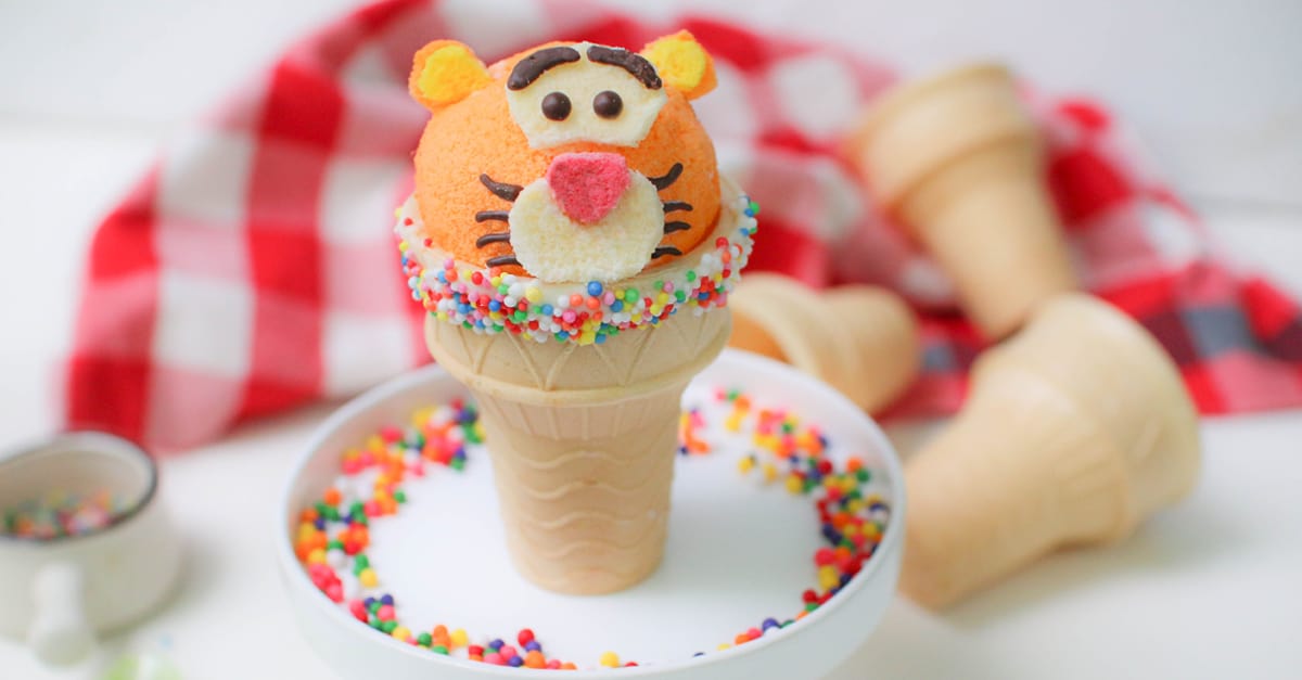 Tiggerific Cupcake Cone featuring a playful Tigger face scoop, rainbow sprinkles, and a festive red checkered backdrop at Disney.