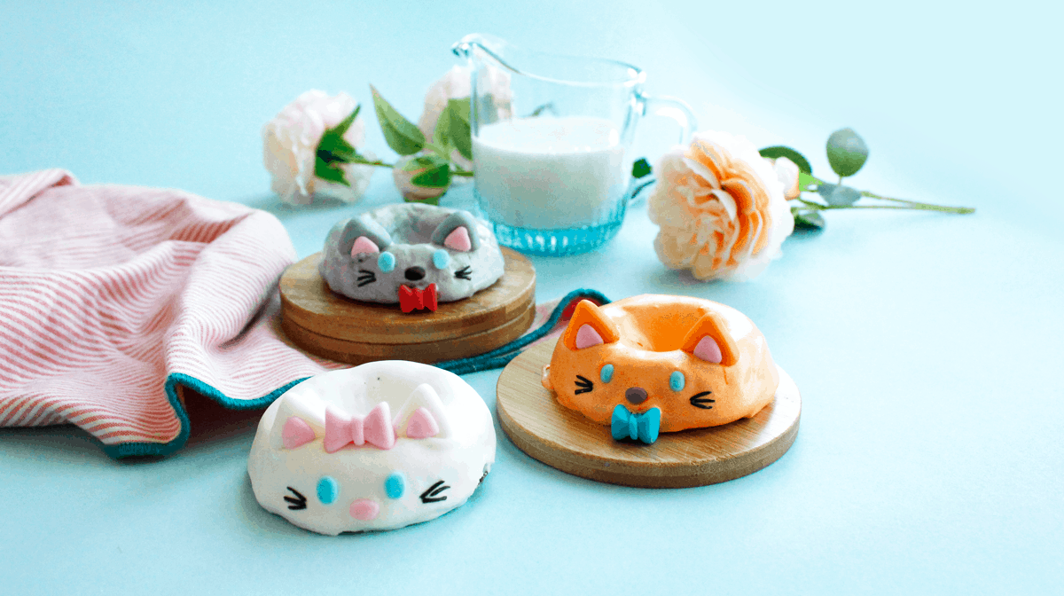 Cat-shaped donuts decorated like Aristocats, with colorful icing, milk, flowers, and a striped towel on Disney-inspired blue.