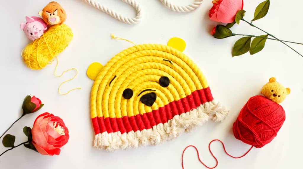 A Winnie the Pooh-inspired yarn art in classic yellow and red, crafted as a playful wall piece, surrounded by Disney decor.