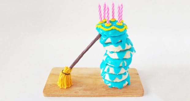 Blue donuts stacked with birthday candles rest against a broomstick on a wooden board, inspired by Sleeping Beauty Castle.