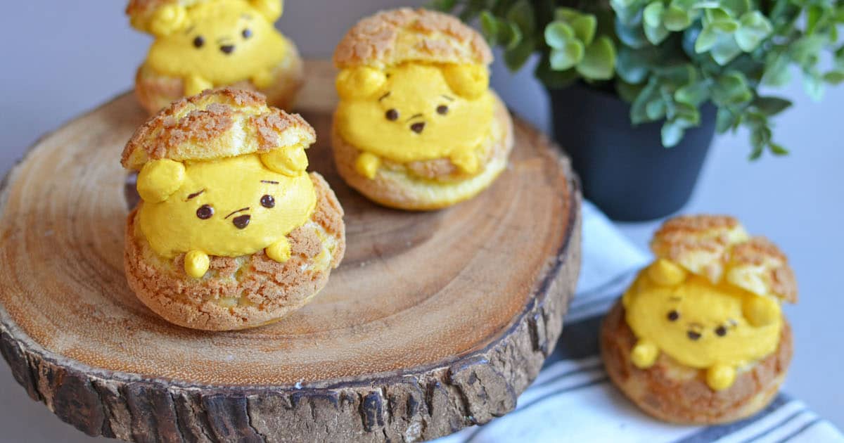 Winnie the Pooh-inspired bear cream puffs are served on a wooden platter, creating a magical Disney treat near lush greenery.