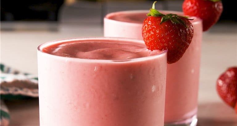 Two glasses of pink strawberry smoothie with fresh berry garnishes, a treat fans would love at Disneyland, just like a Strawberry Dole Whip.