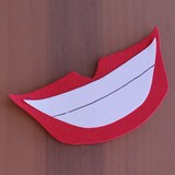 Ursula’s iconic red-lipped, toothy grin paper cutout, great for Disney-themed crafts, displayed on a brown backdrop.