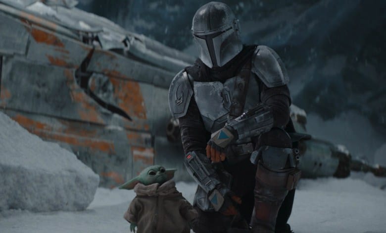 The Mandalorian kneels with Grogu on snowy terrain beside a crashed ship, recreating a Season 2 moment from the Disney+ series.
