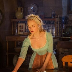 Cinderella, wearing her signature blue dress and apron, tidies up a table inside a cozy, storybook-style kitchen, all aglow with warm light.