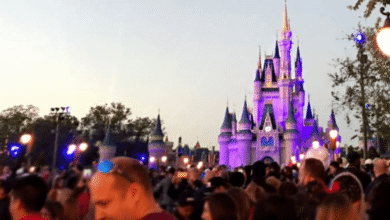 A large crowd at Walt Disney World gathers at dusk in front of Cinderella Castle