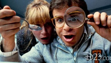 A man looking through a magnifying glass and a woman holding a spoon peer excitedly at something small off-camera, both with surprised expressions—just like scenes from Motivational Disney Movies. The D23.com and Disney logos appear in the corner.